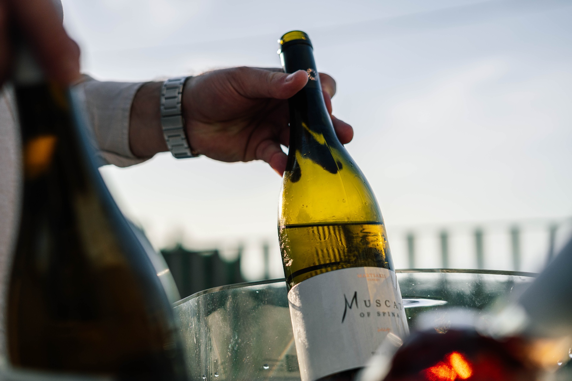A host opening a bottle of Cretan Muscat of Spina at sunset